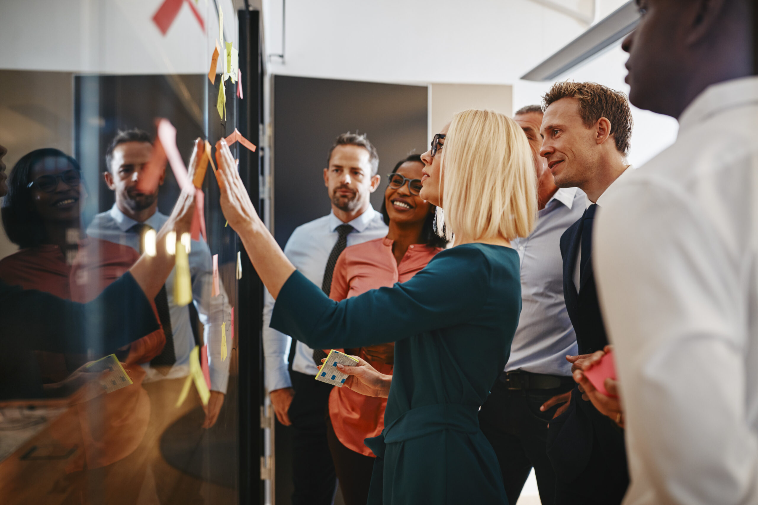 Young businesswoman and her diverse team brainstorming with sticky notes on a glass wall while working together in a modern office