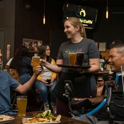 Disabled person enjoying dinner with a male friend and talking to waitress.