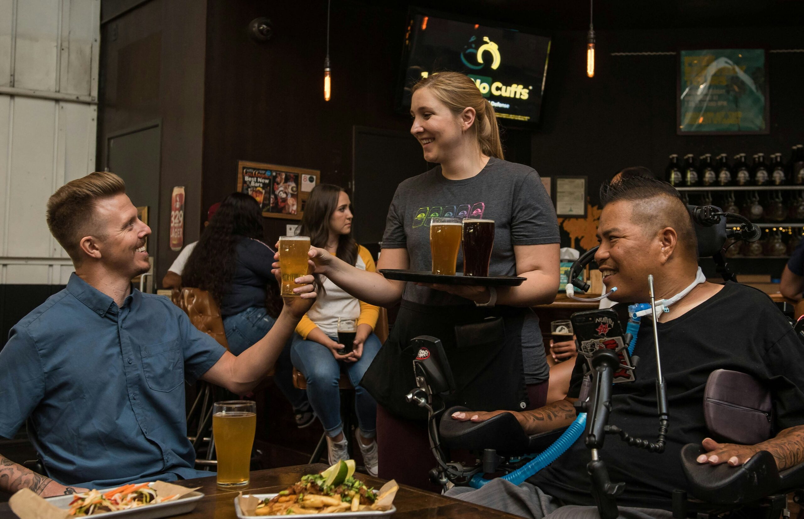 Disabled person enjoying dinner with a male friend and talking to waitress.